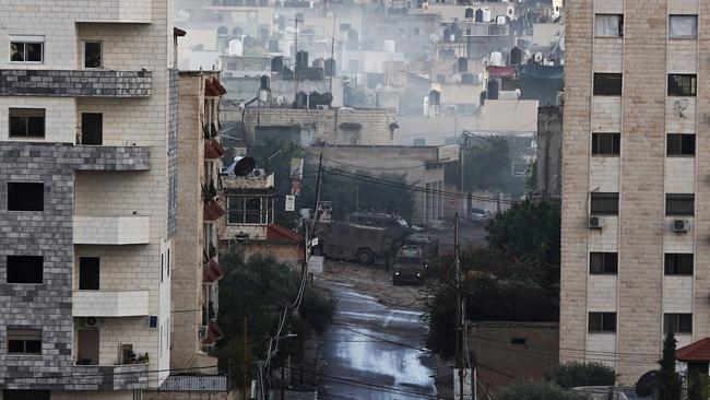 An ambulance drives down a deserted road as Israeli soldiers take position in armoured vehicles at the Jenin refugee camp in Jenin in the occupied West Bank. Picture: AFP