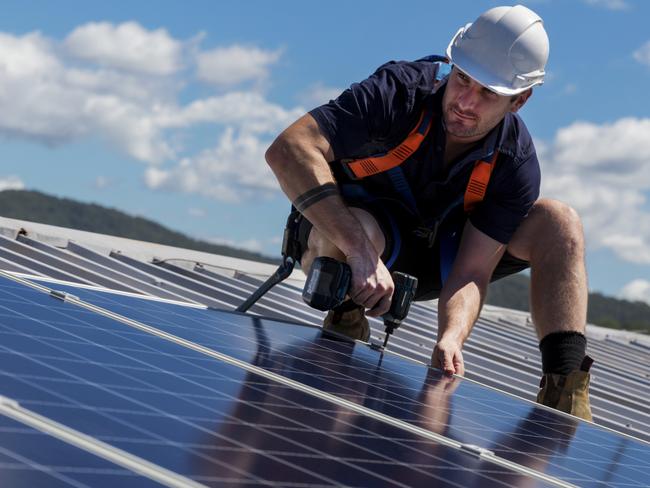 TRADESMAN/ TRADIE/BUILDING INDUSTRY:  Solar panel installer with drill installing solar panels on roof on a sunny day