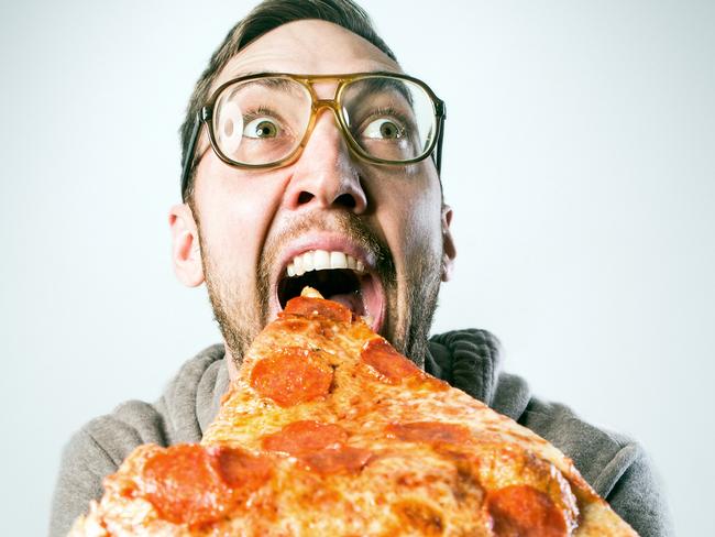 An excited adult man gets ready to take a bite out of a ridiculously large slice of pepperoni pizza, a look of excitement and joy on his face. Horizontal image with copy space.