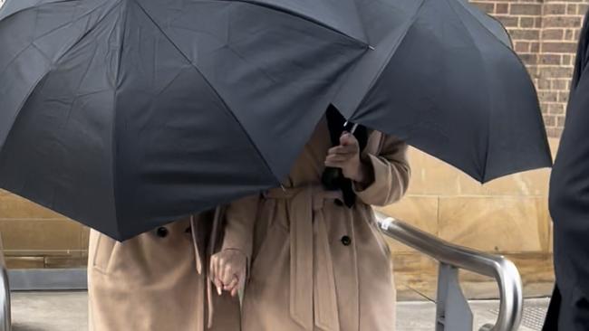 Grace and Lara Buttriss in matching outfits while hiding behind an umbrella exiting Picton Courthouse. Picture: Annie Lewis