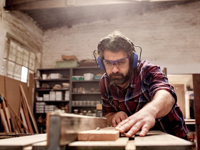 Skilled carpenter and small buiness owner working in his woodwork workshop, using a circular saw to cut through a wooden plank