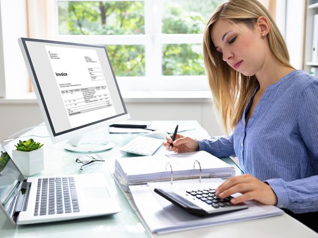 A woman at a desk with a calculator and computer and laptop with receipts. Picture: iStock.