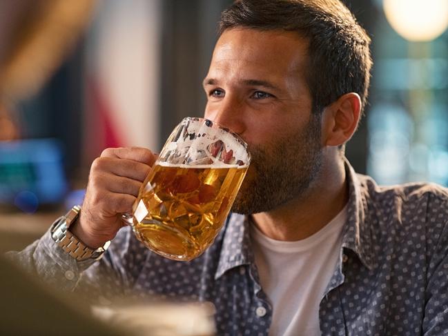 Handsome young man drinking a pint of beer while looking away. Cheerful mid man in casual clothing feeling relaxed while enjoying draft beer in bar. Middle aged guy take a sip from his drink at pub during the night.