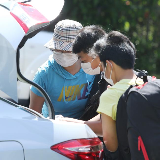 A mother fits out her boys in masks and gloves on their arrival from an Epping Boys High school camp. John Feder/The Australian