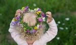 Menina pequena com cabelo loiro encaracolado, usando uma grinalda colorida feita de várias flores selvagens. Vista traseira. Feliz humor de Verão, cores brilhantes, fundo verde grama