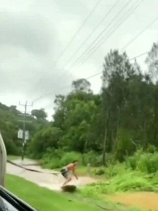 A man attempts to surf behind the back of a car.