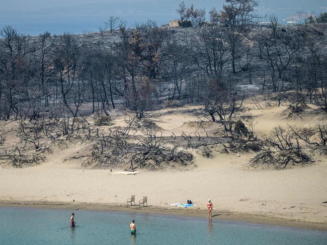 Scorched earth. A woman enters the sea where wildfires have destroyed the woods, in the southern part of the Greek island of Rhodes. Wildfires have been raging in Greece amid scorching temperatures, forcing mass evacuations in several tourist spots. Picture: Angelos Tzortzinis/AFP