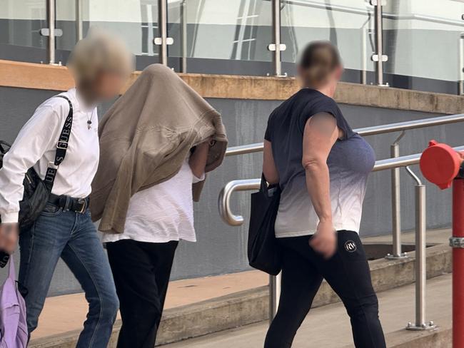 Cheryl Anne Johnston, 62, (centre, covering her head with clothing) walking out of Rockhampton courthouse.