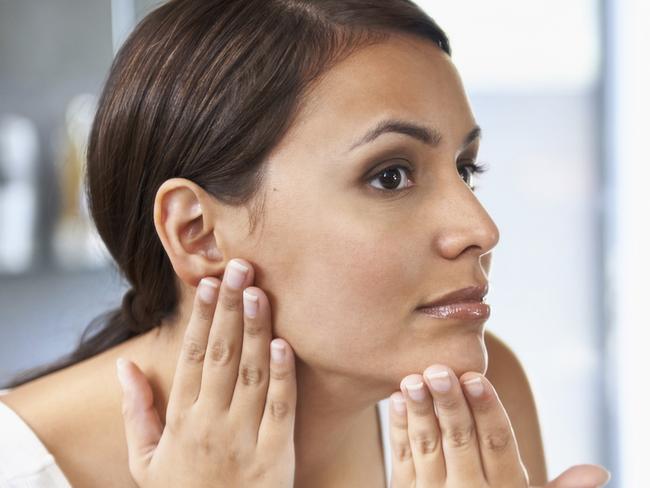 A beautiful young woman looking at her face in the mirror