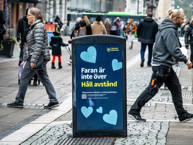 People walk past a rubbish bin with a sign reading “The danger is not over — keep your distance” in a pedestrian street in central Uppsala, Sweden. Picture: AFP