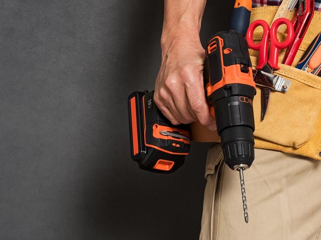 Close up of handyman holding a drill machine with tool belt around waist. Detail of artisan hand holding electric drill with tools isolated over grey background. Closeup hand of bricklayer holding carpentry accessories.