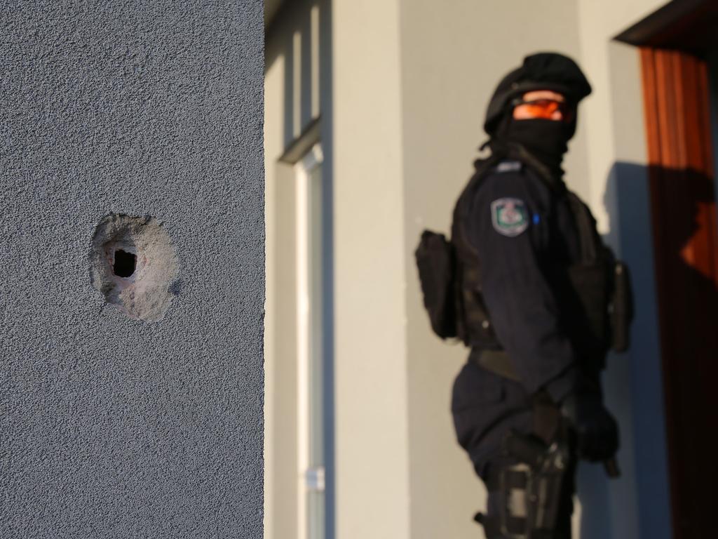 A NSW police officer stands behind a bullet hole in a wall after an attempted shooting murder in western Sydney on Tuesday. Picture: AAP Image/Supplied by NSW Police 