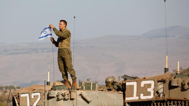 An Israeli soldier places a national flag atop a Merkava tank during in a military drill near the border with Lebanon. Picture: AFP