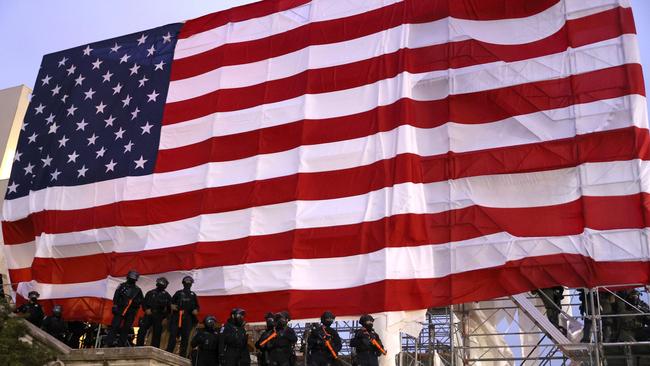 Police officers in riot gear stand under a large American flag as protesters gather. Picture: AFP.