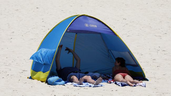 Beachgoers go to extreme lengths to avoid the sun in a scorching heatwave on Broadbeach at the Gold Coast. Picture: Tertius Pickard