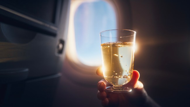 Man enjoying a drink during a flight. Passenger holds up a glass of sparkling wine to the window of an airplane.