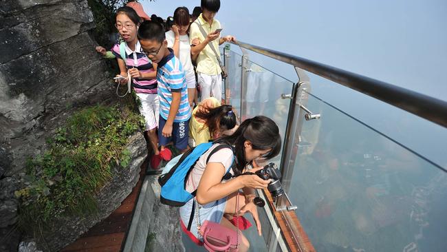 Tourists peer over the edge of the Coiling Dragon Cliff skywalk that has just opened to the public in Hunan province, China. Picture: Shao Ying/Imagine China