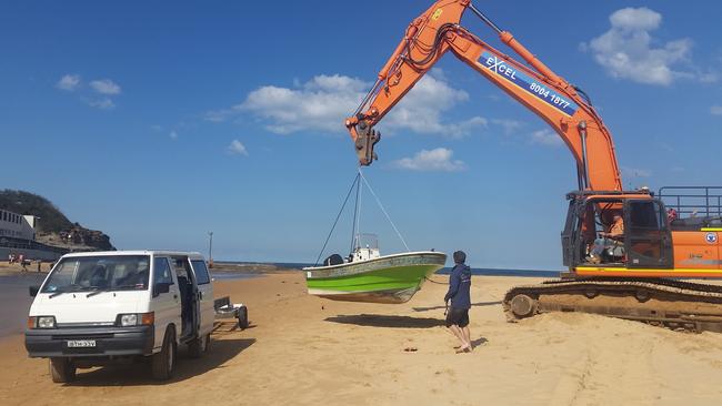 Northern Beaches Council contractors helped put the washed up boat onto a trailer at North Narrabeen Beach. Picture: Lewis Slarke