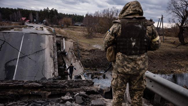 An Ukrainian serviceman looks at a civilian crossing a blown up bridge in a village, east of the town of Brovary. Picture: AFP.