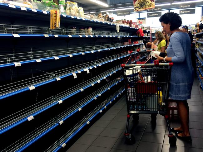 Dire ... Shoppers stand in an aisle with empty shelves in a supermarket in Athens. Picture: AFP/ARIS MESSINIS