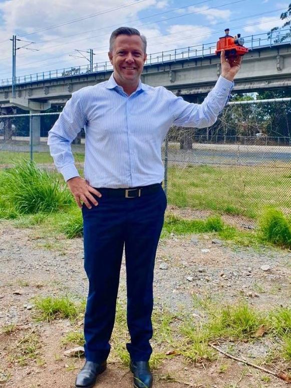 Councillor Cameron Caldwell holding up a toy train at the Helensvale North railway station site.