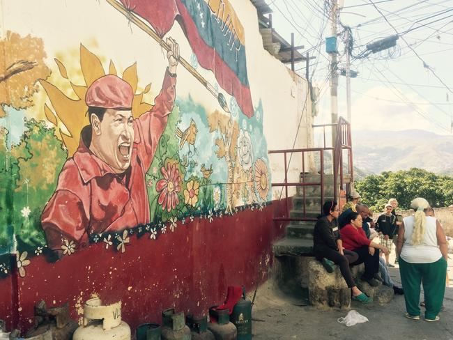 Locals gather around a mural of former president and leader of the socialist revolution, Hugo Chavez. Picture: Courtesy of the ABC