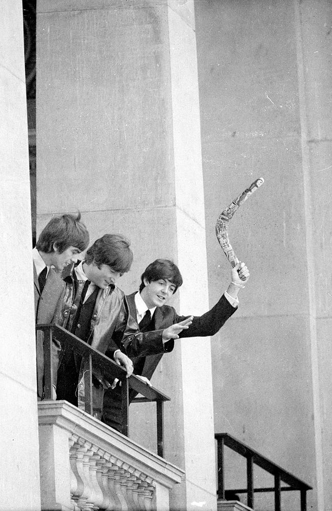Paul McCartney waves a boomerang on the balcony of the Town Hall as John Lennon and George Harrison look down at the fans.