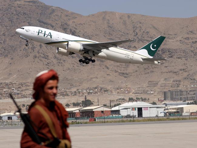 (FILES) In this file photo taken on September 13, 2021, a Taliban fighter stands guard as a Pakistan International Airlines plane, the first commercial international flight to land since the Taliban retook power last month, takes off with passengers onboard at the airport in Kabul. - Few nations endured as tumultuous a year as Afghanistan in 2021, and the country's woes are far from over as a bitter winter draws in. (Photo by Karim SAHIB / AFP)