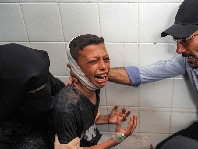 TOPSHOT - A woman and a man comfort an injured boy mourning the loss of his father who was killed in the aftermath of overnight Israeli bombardment in al-Maghazi in the central Gaza Strip, at the morgue of the Aqsa Martyrs hospital in Deir el-Balah on June 25, 2024 amid the ongoing conflict in the Palestinian territory between Israel and Hamas. (Photo by Bashar TALEB / AFP)