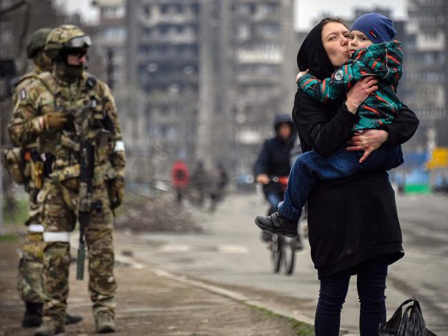 A woman holds a child next to Russian soldiers in a street of Mariupol. Picture: Alexander Nemenov/AFP