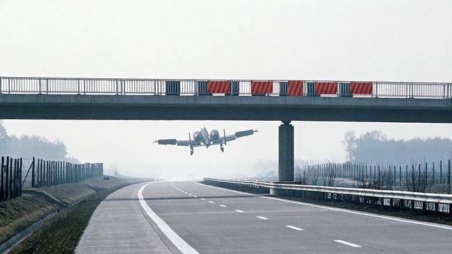 An A-10 Thunderbolt II aircraft lands on a German autobahn in the 1980s just past an overpass.