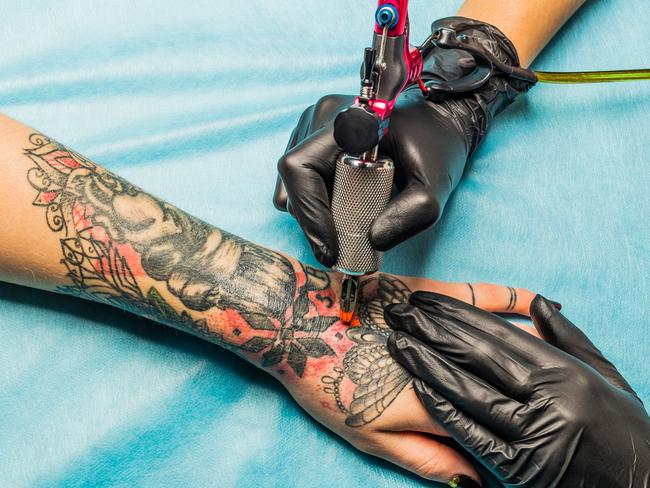 Close up tattoo artist demonstrates the process of getting black and red tattoo with orange paint. Master works on the professional blue mat in black sterile gloves.  - Picture istock