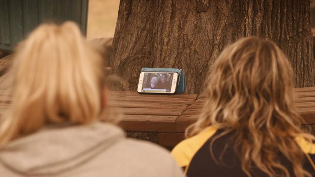 Holiday visitors crowd around a mobile phone to hear the latest on the fires around them at the Mallacoota Beachcomber Caravan Park. Picture: David Caird