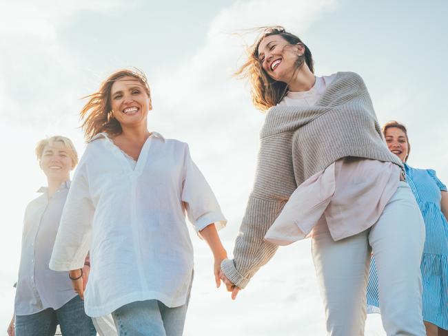 Portrait of four cheerful smiling women holding hand in hand walking by a high green grass meadow. They looking at the camera. Woman's friendship, relations, and happiness concept image.