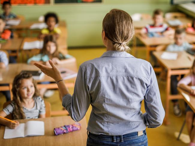 Back view of a female teacher teaching large group of elementary students in the classroom.