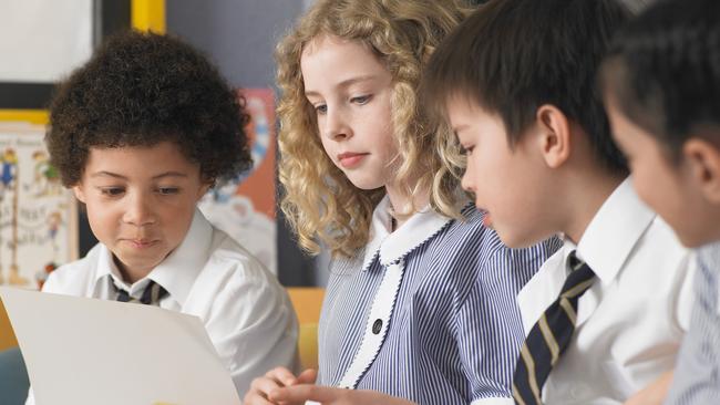 Row of school students reading book sitting in classroom. Source: iStock