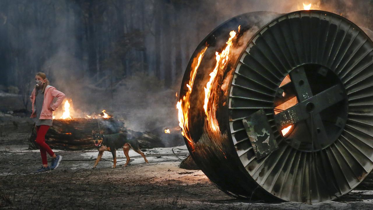 A girl walks her dog passed burning spools of NBN cable in Mallacoota during the recent bushfires. Picture: David Caird