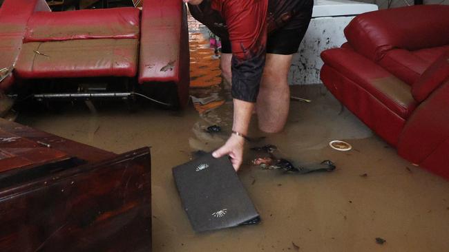 A monsoonal tropical low pressure system has brought devastating widespread flooding to North Queensland and parts of Far North Queensland, with over 1000 millimetres of rain recorded in some areas. Clitheroe Street resident Tracy Ebert pics up a sodden photo album from her lounge room floor, after flood water inundated her Cardwell home overnight. Picture: Brendan Radke