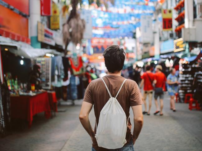 Rear view image of a young man, solo traveler, walking in the Chinatown district of Kuala Lumpur, Malaysia. He is wearing a white rucksack, enjoying walking and shopping in Malaysia capital.