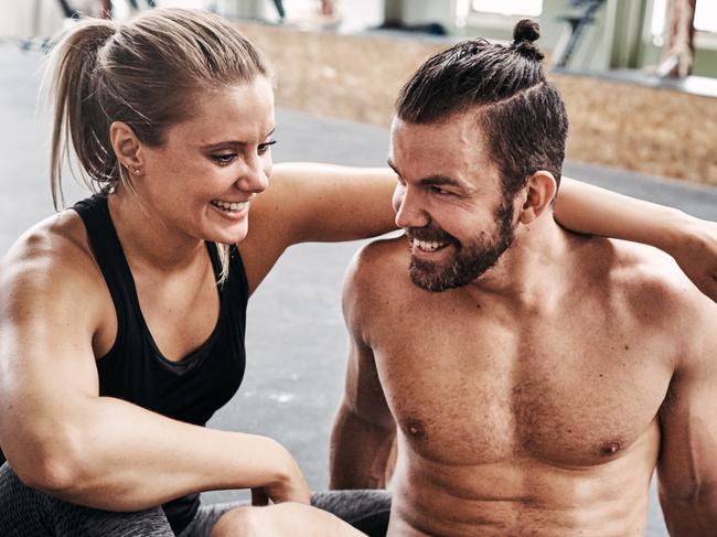 Fit young couple in sportswear laughing while sitting together on a gym floor taking a break from working out