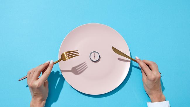 Round watch of six o'clock and woman's hand with fork and knite in agirl's hands on a blue background with shadows. Time to lose weight, eating control or diet concept. Place for text.