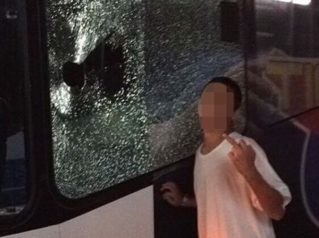 A school-aged child poses next to a smashed bus window.