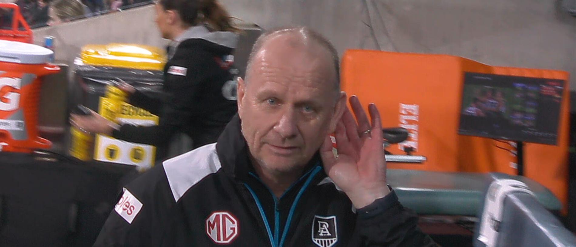 Ken Hinkley appears to put his hand to his ear listening to the quiet Geelong crowd.