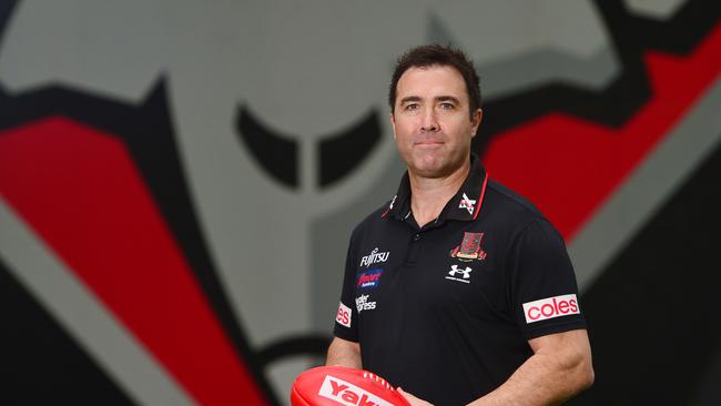 Essendon coach Brad Scott in front of the Bomber logo.