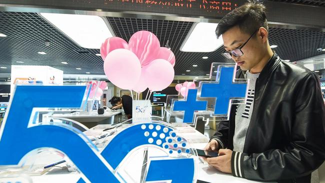 A customer looks at a mobile phone next to a 5G logo at a store in Hangzhou, China. Picture: AFP