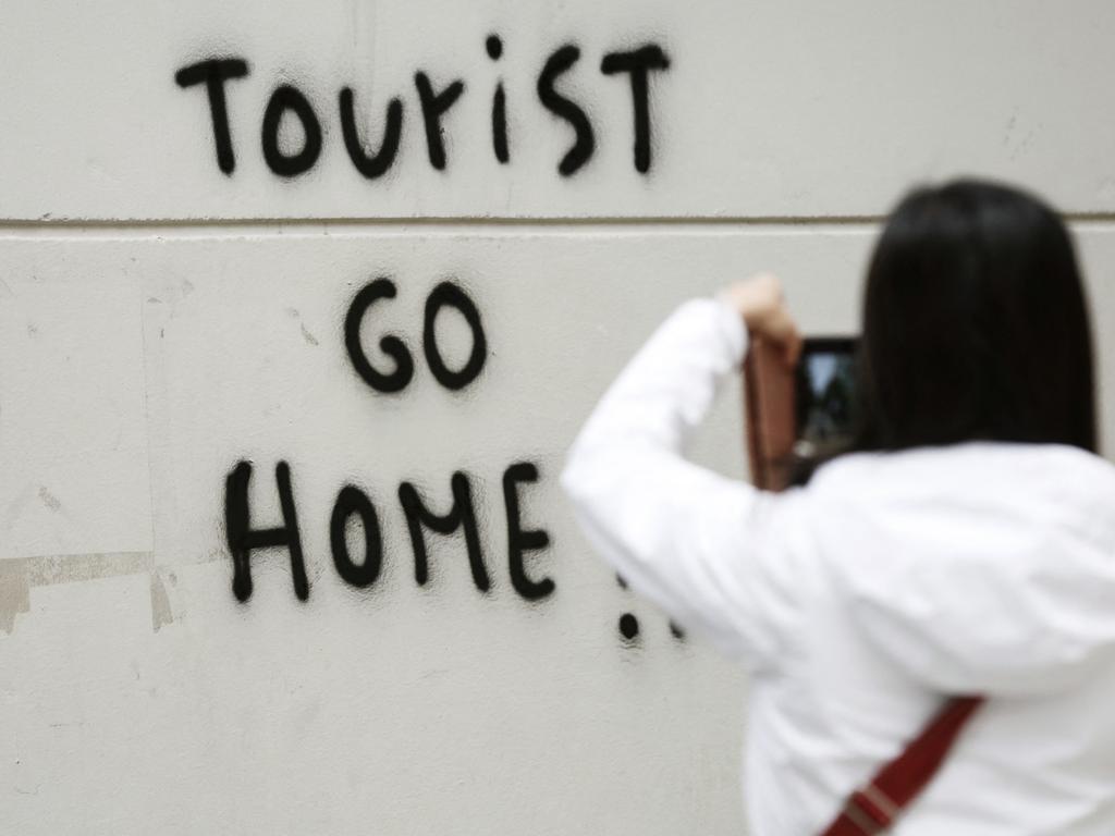 A tourist takes a picture of a tag reading ‘Tourists go home’ on her way to Guell Park in Barcelona on November 2, 2018. Picture: Pau Carrena / AFP