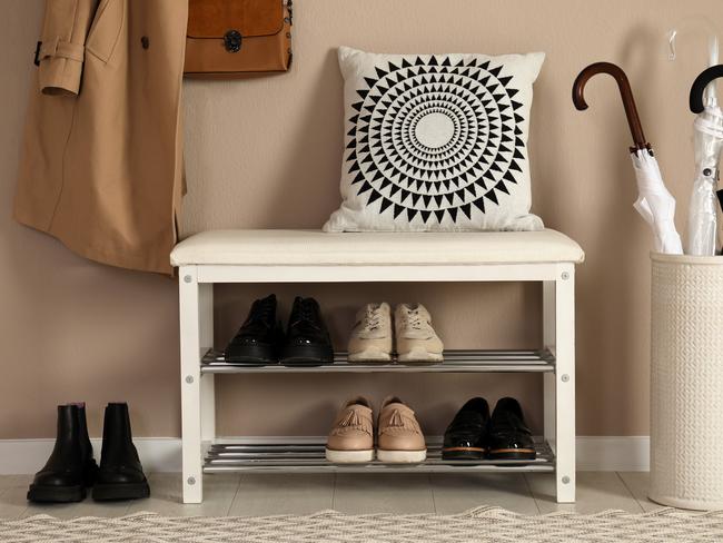 Stylish storage bench with different pairs of shoes near beige wall in hall