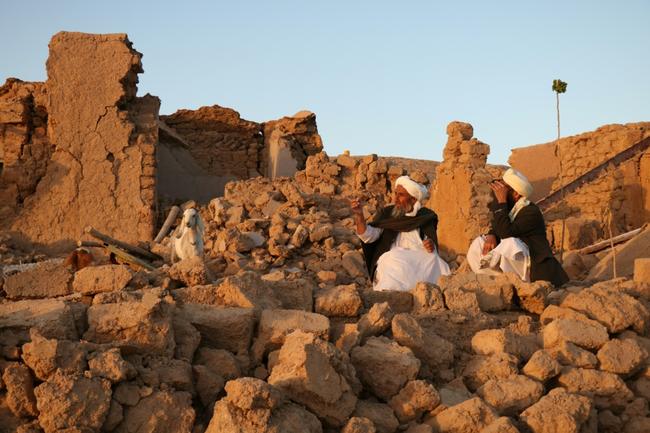 Afghan men sit in the rubble of their flattened homes in Sarbuland village in Herat province following an earthquake