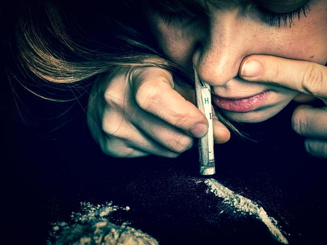 Junkie woman snorting cocaine powder with rolled banknote on black background