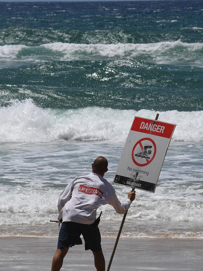 A lifeguard places a danger sign on the Gold Coast, Wednesday, February 20, 2019. Huge swells and high tides are set to pummel south-east Queensland beaches over the coming days as Cyclone Oma tracks towards the Queensland coast.. Photo: Dave Hunt/AAP.